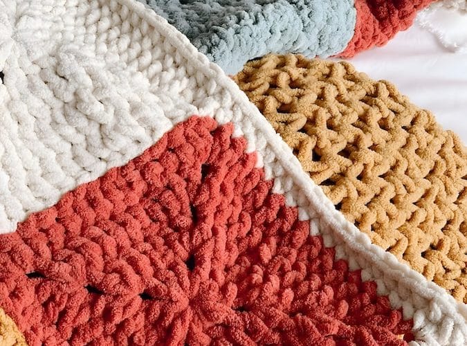 a person holding a crocheted blanket on top of a bed